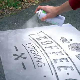 A plastic stencil is used to apply a chalk spray motif on the ground.